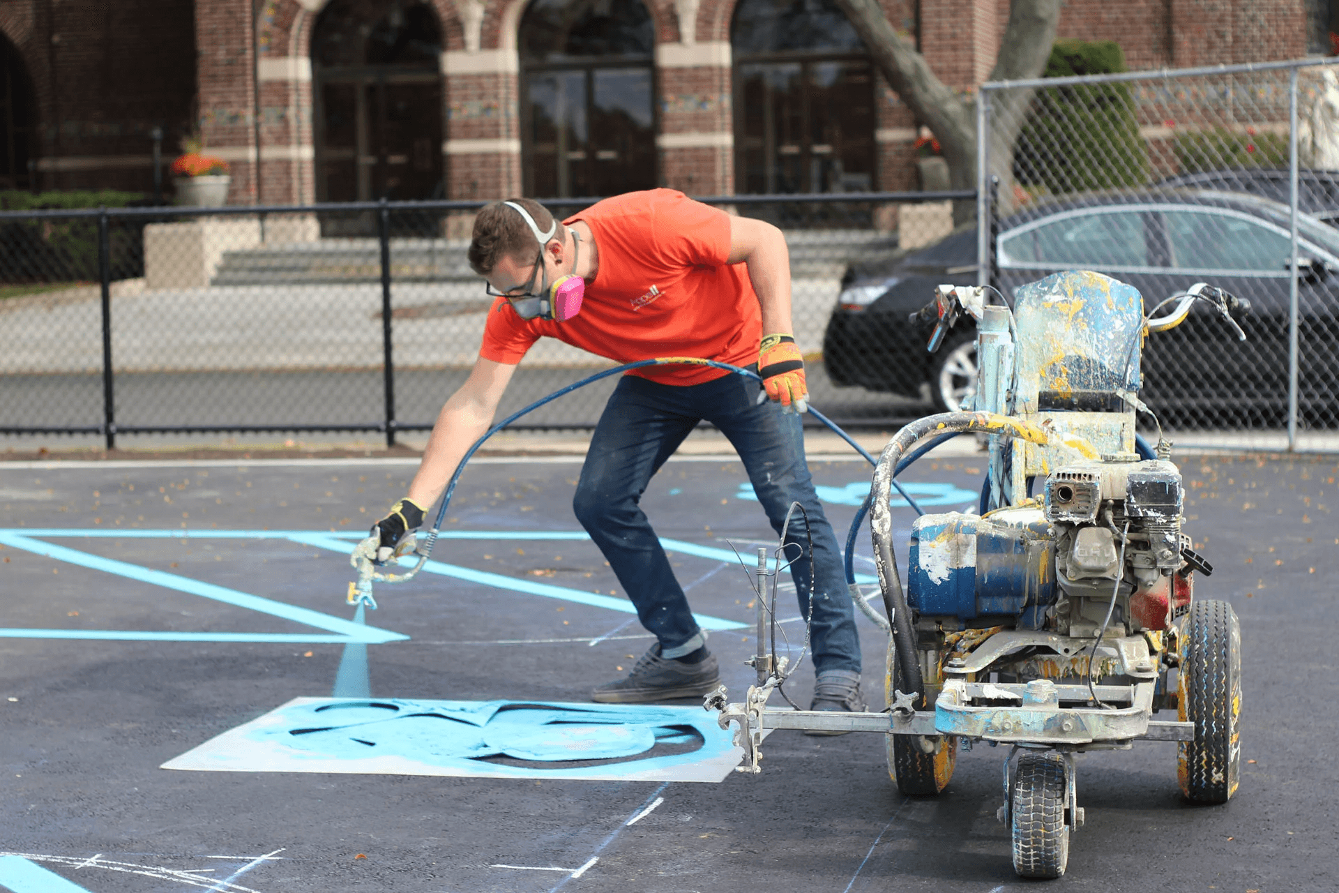 Process 03 A person using a paint sprayer to apply blue paint to a sports court surface.