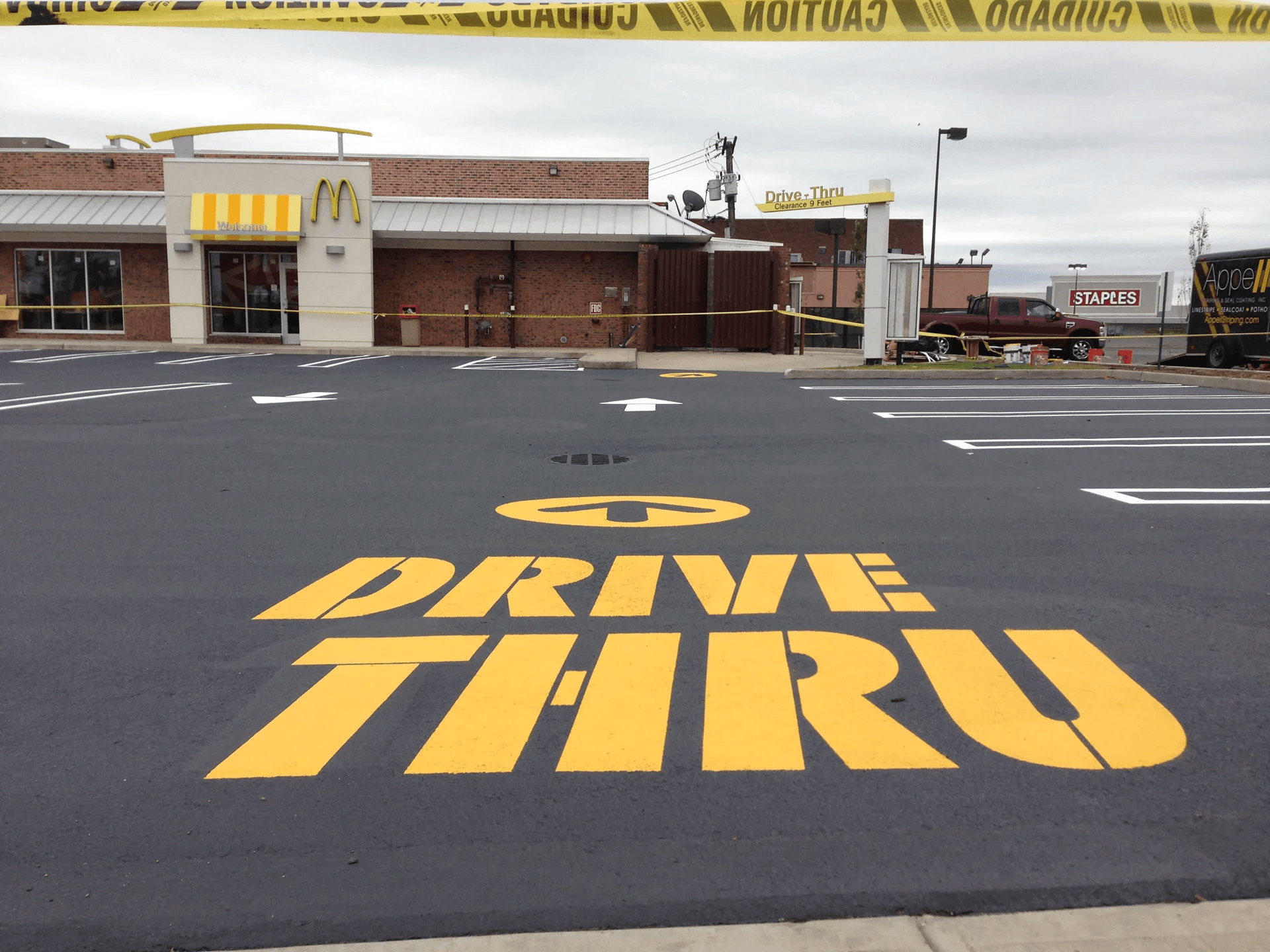 Process 04 A McDonald's drive-thru area with a large 'Drive-Thru' sign painted on the asphalt, bordered by caution tape.