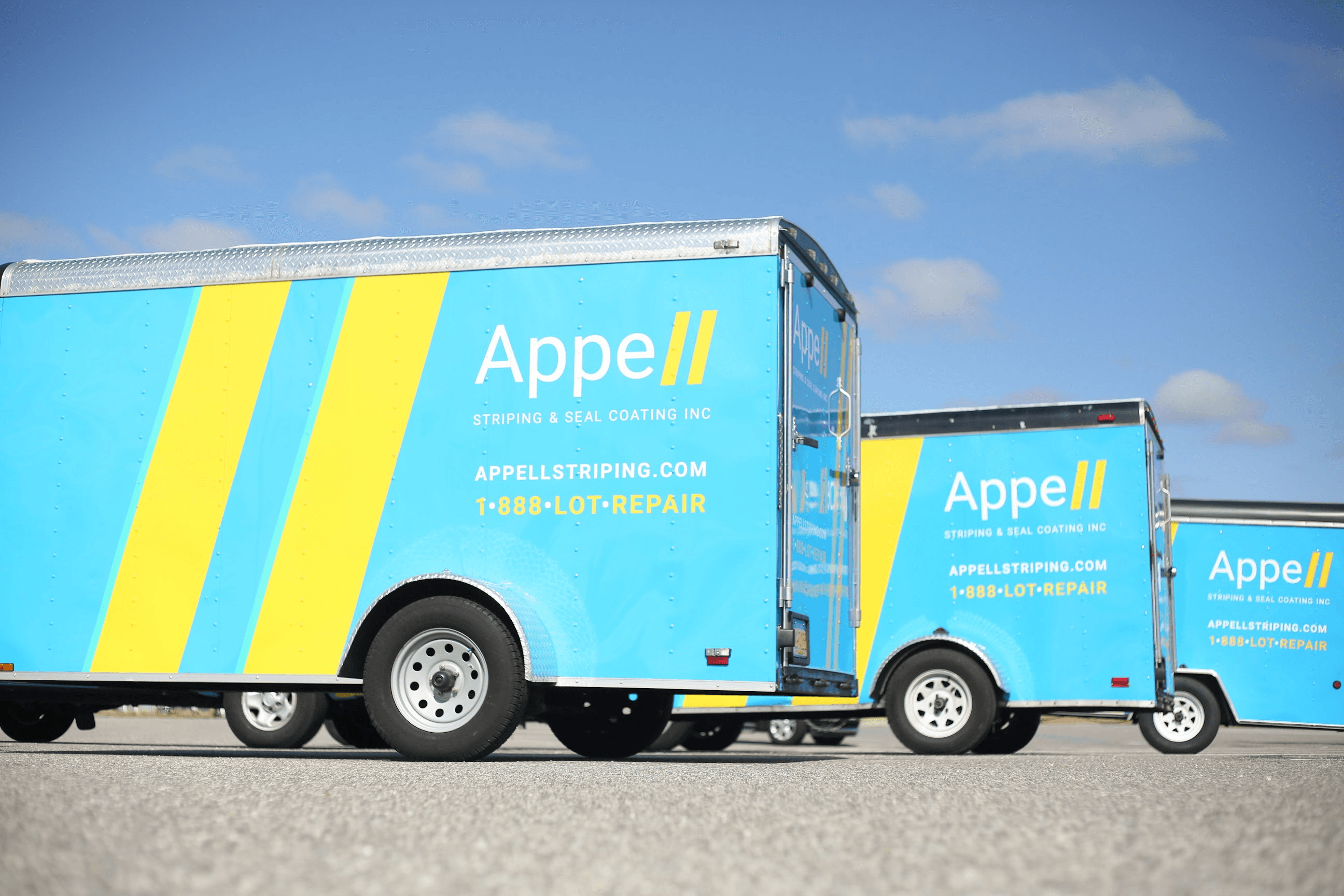 The investments Two blue and yellow Appell Striping trailers parked under a clear sky, showcasing the company's branding and services.